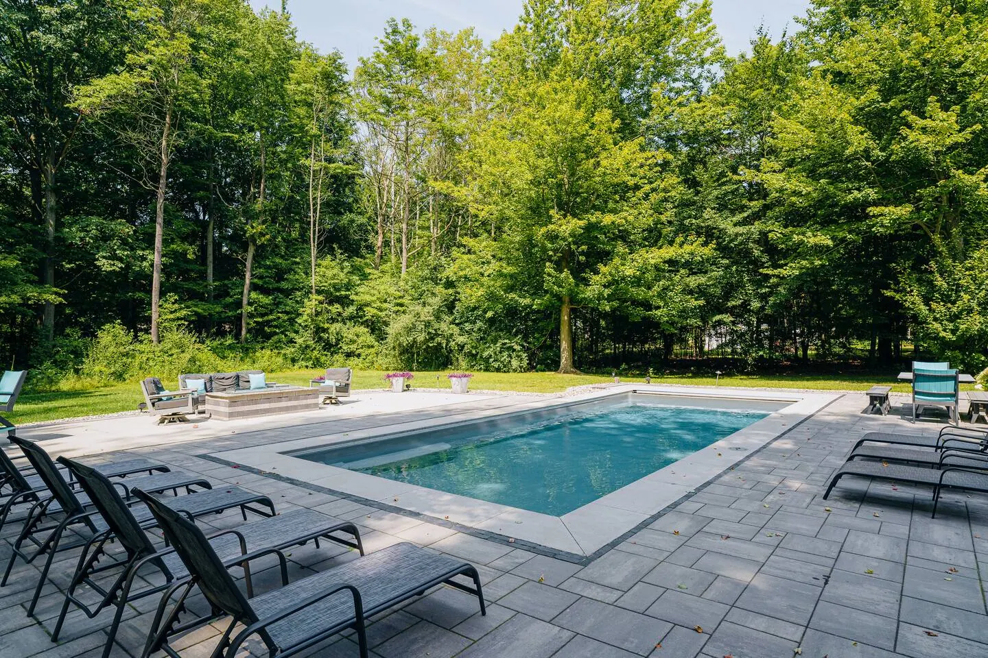 Pool water and patio with lounge chairs facing the woods
