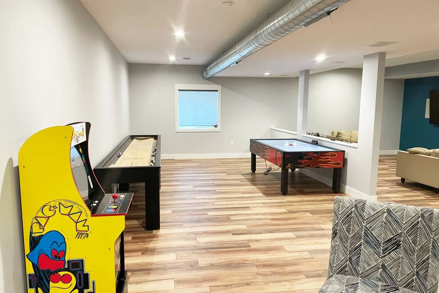 Basement game room with a Pac-Man arcade cabinet and shuffleboard table