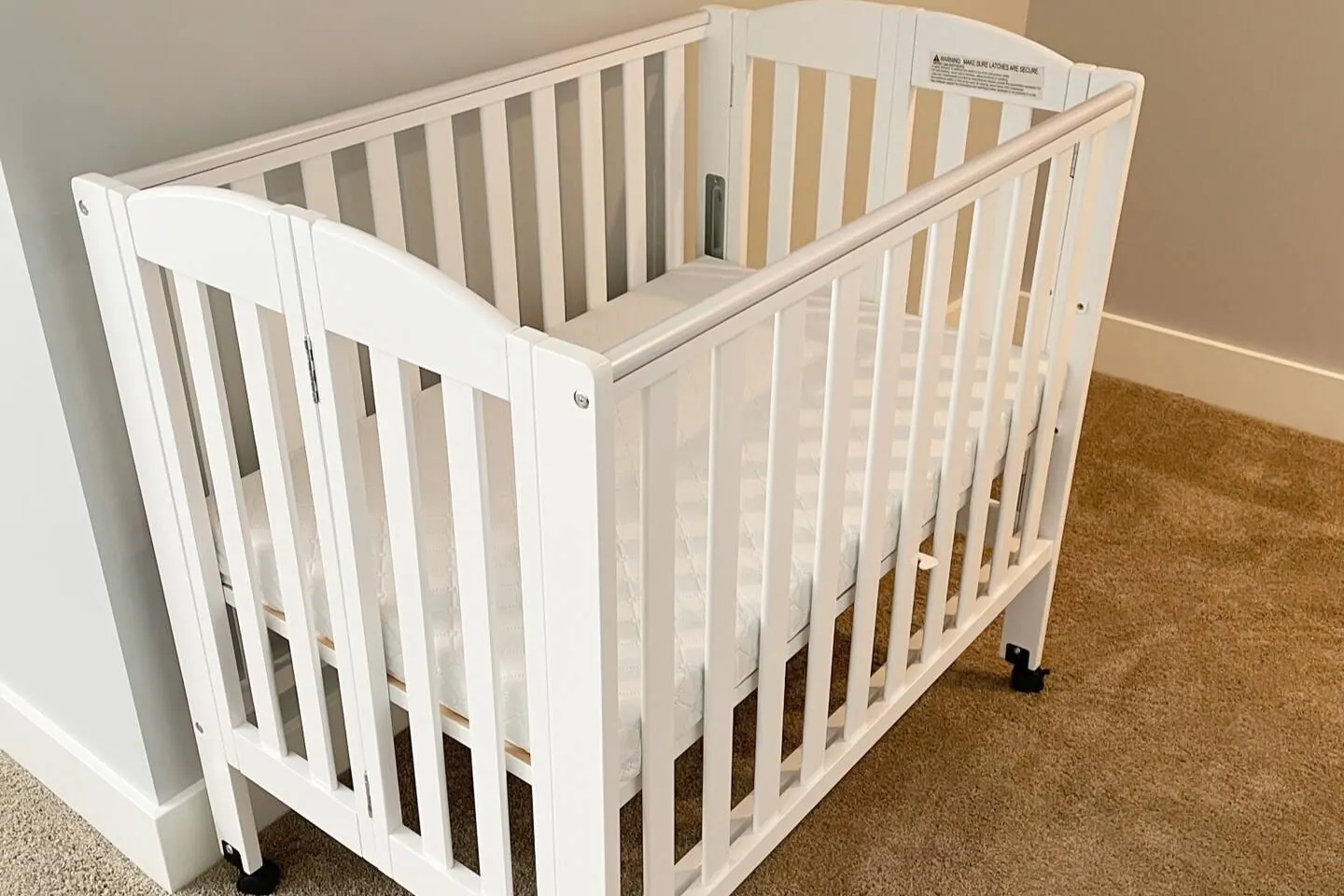 White folding crib set up in a carpeted bedroom